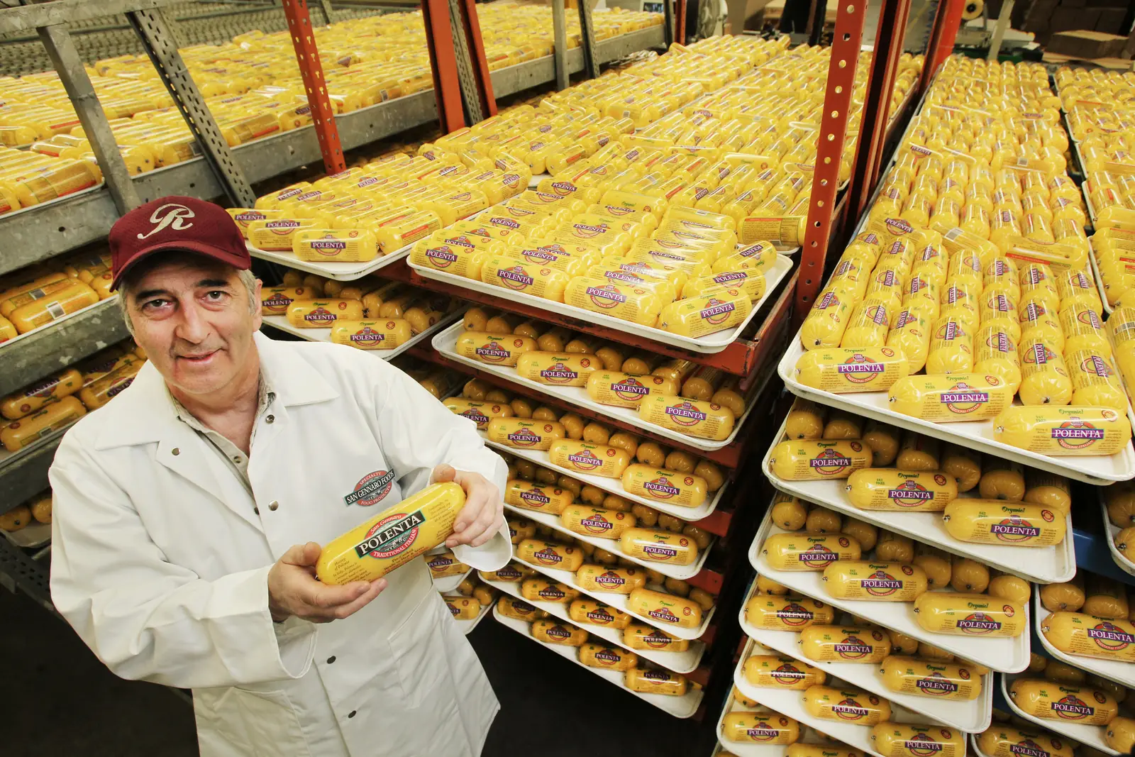 Jerry Mascio holds a roll of polenta in front of racks of polenta trays.