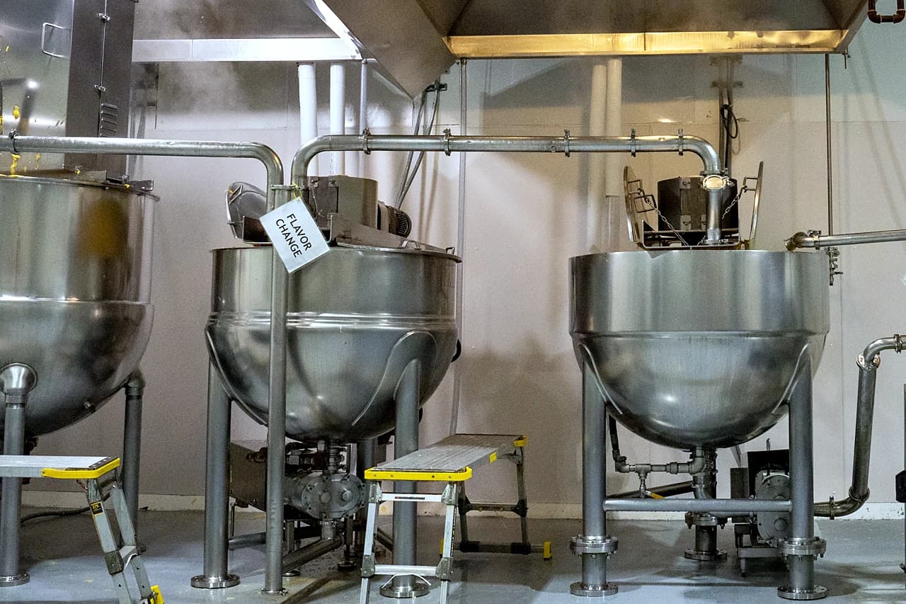 Three steel kettles under exhaust hoods in the kettle room at San Gennaro's Kent plant.