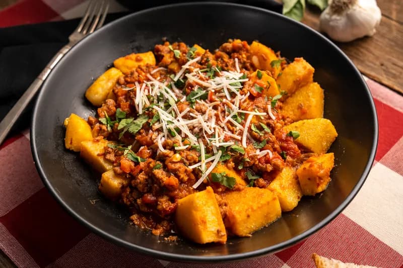 Polenta cubes with Bolognese and parmesan in a black bowl.